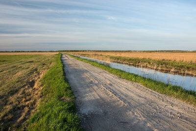 Dirt road amidst field against sky