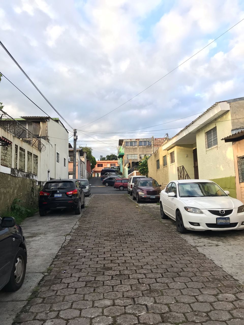 mode of transportation, building exterior, transportation, car, motor vehicle, architecture, city, built structure, cloud - sky, land vehicle, street, building, the way forward, direction, sky, residential district, day, road, nature, cobblestone, outdoors, no people, paving stone