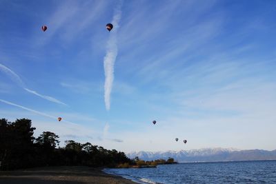 Scenic view of contrails by airliners and vivid colored balloons in winter blue sky above lake