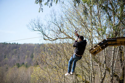 Man hanging on zip line by trees at forest