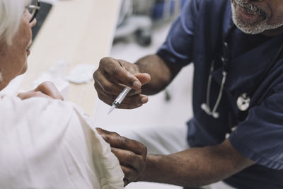 Male doctor injecting senior female patient in medical clinic