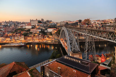 Bridge over river by buildings in city against sky during sunset