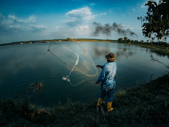 Rear view of fisherman throwing fishing net in lake