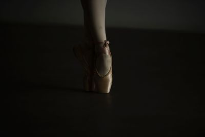 Low section of ballet dancer dancing on floor in darkroom