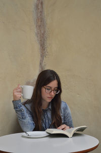 Young woman reading book while having coffee at table