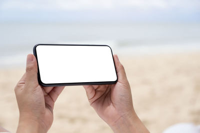 Midsection of person holding mobile phone in sea