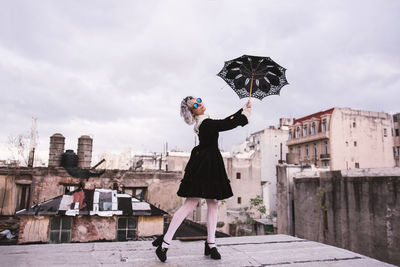 Woman holding umbrella against buildings in city