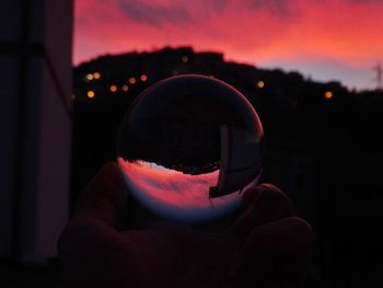 Close-up portrait of person holding crystal ball against sky during sunset