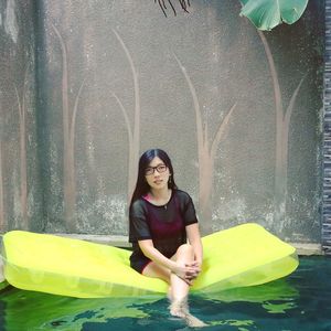 Full length of young woman sitting against water