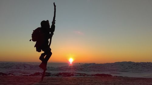 Silhouette woman climbing on pole at beach against sky during sunset