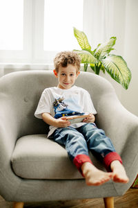 Portrait of boy holding phone sitting on sofa at home