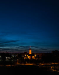 Illuminated buildings against blue sky at night