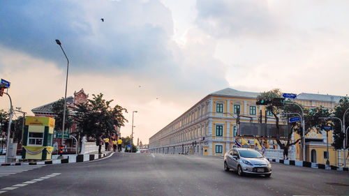 Cars on city street by buildings against sky