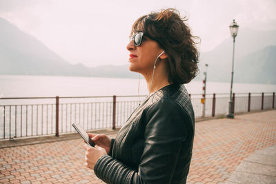 Side view of young woman using mobile phone against river