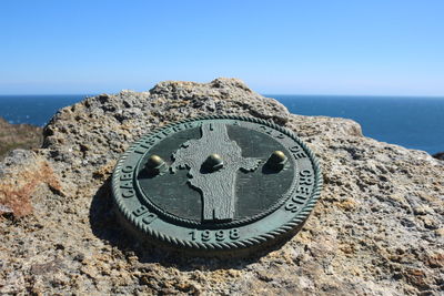 Metallic benchmark on rock at cap de creus against clear sky