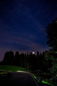 Road amidst trees against sky at night