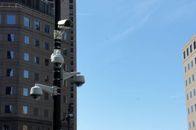 Low angle view of buildings and security cameras against sky