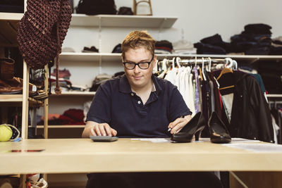 Young man calculating while sitting at checkout counter in clothing store