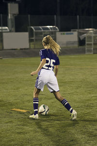 Rear view of girl playing soccer on field at night