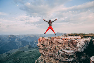 Low angle view of person jumping on rock against sky