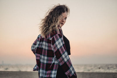 Midsection of woman standing by sea against sky during sunset