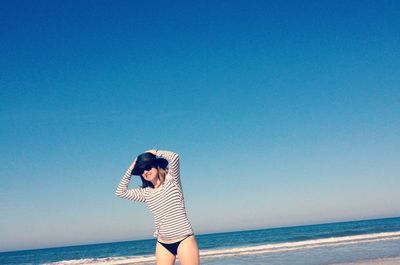 Young woman standing on beach against clear blue sky