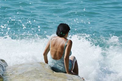 Rear view of shirtless man on rock at sea