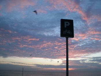 Low angle view of road sign against cloudy sky