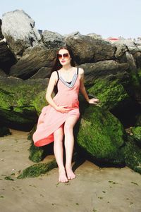 Portrait of beautiful young woman standing on rock at shore