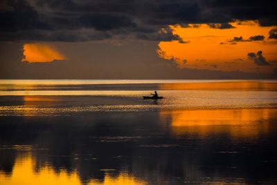 Silhouette man rowing boat in sea against sky during sunset