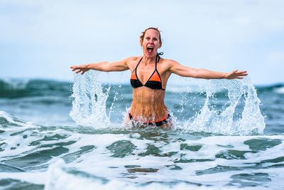 Full length of young woman standing in sea against sky