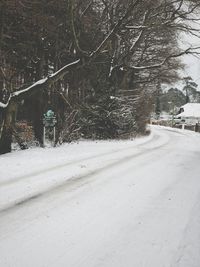 Snow covered road by trees in city