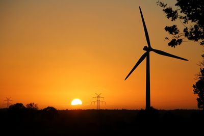 Silhouette windmill on field against romantic sky at sunset