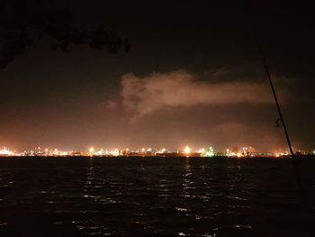 Illuminated city by sea against sky at night