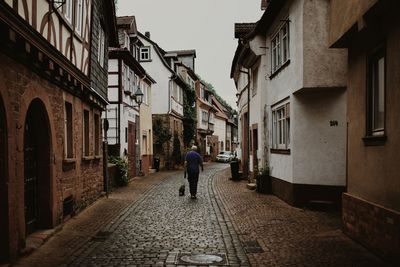 Rear view of man walking on footpath amidst buildings in city