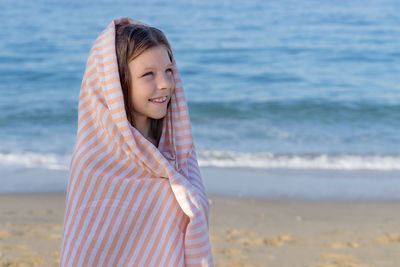 Portrait of a young girl wrapped in a towel against the blue sky and the sea.