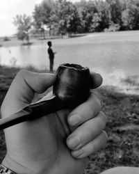 Cropped image of person holding smoking pipe against river