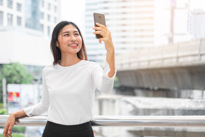 Portrait of smiling woman photographing while standing in city