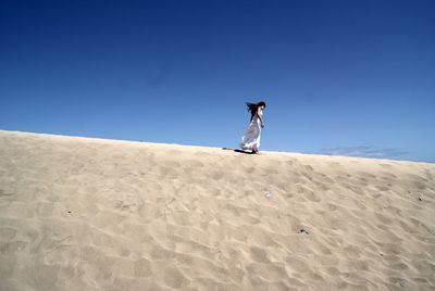 Low angle view of woman walking on sand dune at beach against clear blue sky