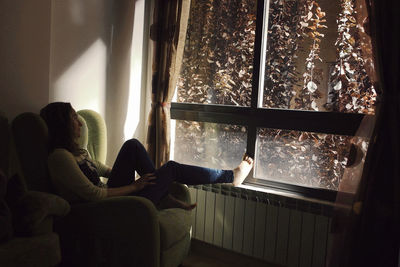 Young woman sitting on armchair by window at home
