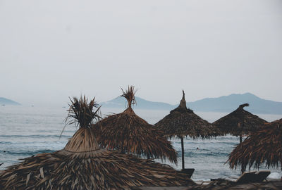 Thatched roof parasols at beach against clear sky