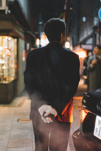 Rear view of man walking on illuminated street at night