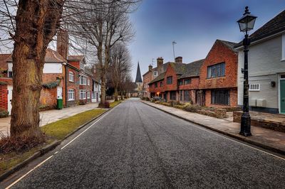 Street amidst bare trees in city against sky