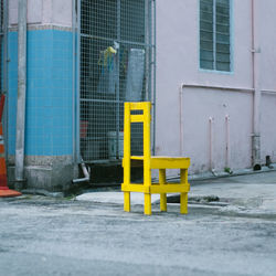 Yellow wooden chair on footpath by building
