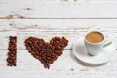 Letter and heart shape made with coffee beans by cup on table