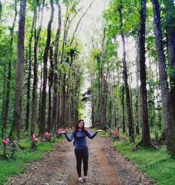 Portrait of woman standing on dirt road amidst trees in forest