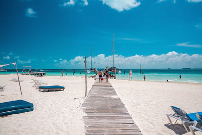 Tourists enjoying beach summer holiday with boats moored on pier