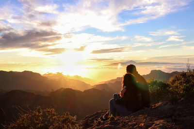 Rear view of man sitting on land against sky during sunset