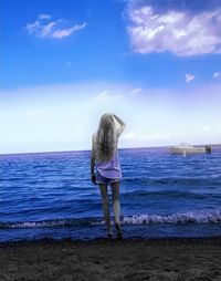 Rear view of woman standing at beach against sky