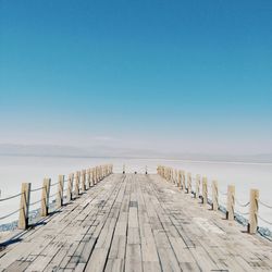 Pier over sea against clear blue sky